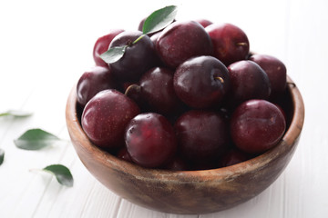 Bowl with fresh ripe plums on white background