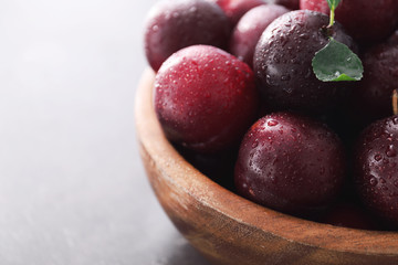 Bowl with fresh ripe plums on light background, closeup