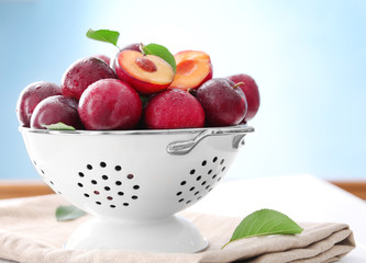 Collander with fresh ripe plums on table