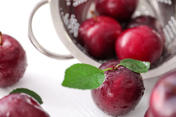 Fresh ripe plums and sieve on white background, closeup