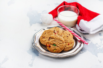 Milk and cookies for Santa Claus and Santa's hat over wooden background. Xmas concept, greeting card. Toned image.