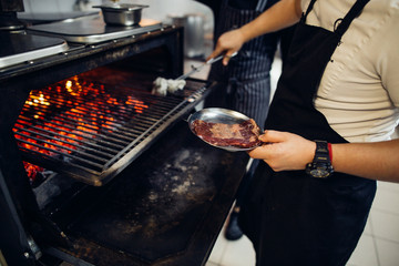 steaks cooking over flaming grill on restoraunt kitchen