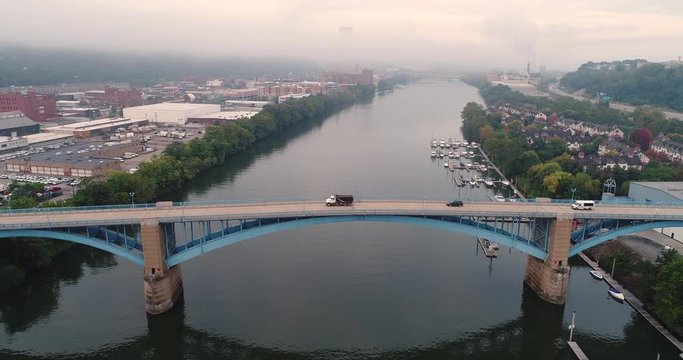 An early morning wide profile aerial establishing shot of traffic passing over the 31st Street Bridge with the foggy Pittsburgh skyline in the distance.  	