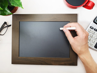 Man sketching on a blank blackboard with coffee and calculator