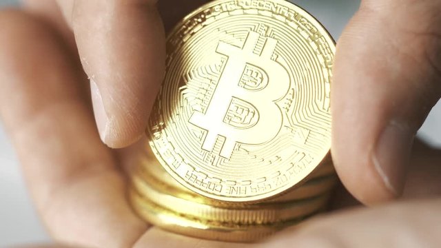 Hand holding a stack of Bitcoin coins and showing one to the camera. Bitcoin is a worldwide cryptocurrency and digital payment system.