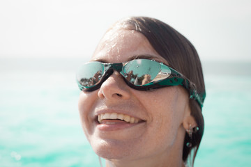 Face of a smiling woman in a swim glasses in a pool