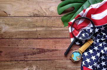 Top view Handkerchief look like USA flag with map watch and Magnifying glass on green leave and wood pattern,  For concept find America on Columbus Day,Have copy space.
 - obrazy, fototapety, plakaty