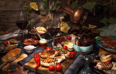 Overhead of dinner table. Assorted grilled barbecue meat and seafood with vegetable. Pork grilled steaks, salmon trout, mussels, shrimps, dried tomato, cherry tomato, chili pepper, glasses of wine.