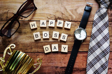 Top view Wood text Happy boss day massage,Necktie,black watch,brown glasses and gold trophy. For...