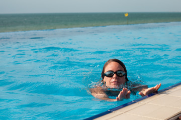 Woman in a swim glasses in a pool with sea view
