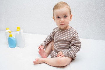 beautiful baby holding a bottle in the hand with shower gel, beside lies Baby cosmetic tubes on white isolated background