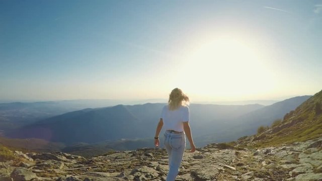 Young beautiful fit lifestyle influencer or blogger, travels around world, inspiring sunset view, hikes or walks on mountain pass summit to enjoy amazing nature, hair blows in wind
