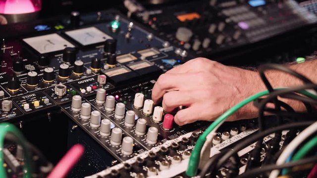 View on hand twisting knobs on mixtape board panel to tune levels of sound. Professional music production in studio concept
