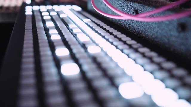 Close up shot of musical audio production equipment, mixing board with multiple changing and blinking lights and buttons in darkness of production wworkstation studio