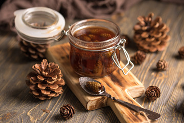 A jar of homemade jam made of pine cones on a dark wooden background.
