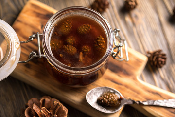 A jar of homemade jam made of pine cones on a dark wooden background.