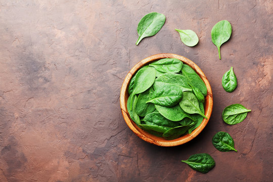Organic food. Baby spinach leaves in wooden bowl on rustic stone table top view. Copy space for text.