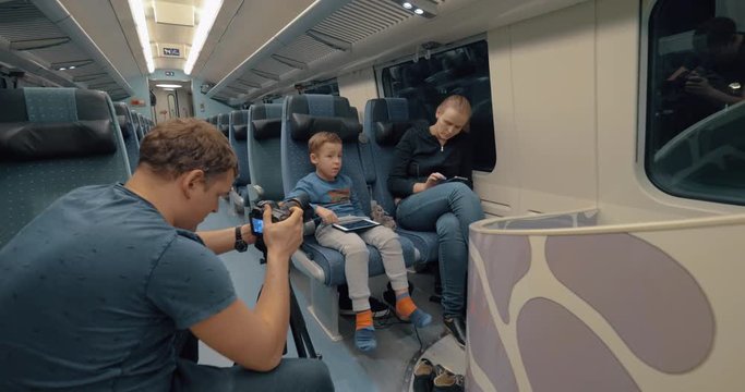Man stocker shooting footage of a mother with son traveling by express train and passing time with pad and cellphone