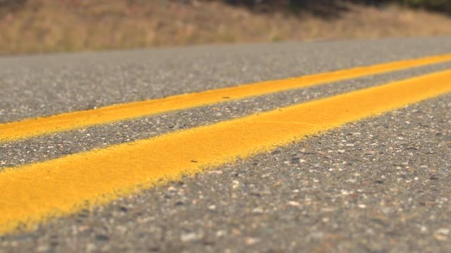 CLOSE UP: Bright double yellow lines on empty interstate road on sunny day. Brand new twin yellow lines on empty highway road in sunny countryside. Yellow doubles on  road surface