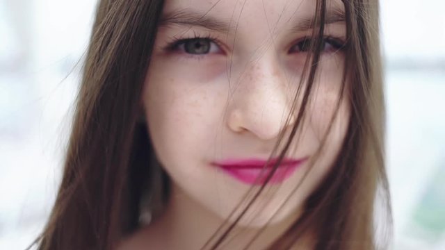 Emotional portrait of a young girl with a stern and thoughtful look of the camera on a light natural background.