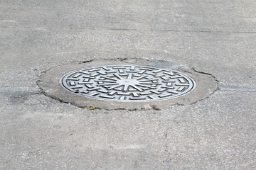 Manhole cover on the street surrounded by asphalt.