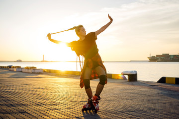 Young stylish funky girl with green hair riding roller skates and dancing near sea port during...