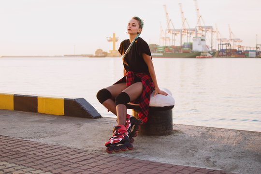 Young stylish funky girl with green hair with roller skates near sea port during sunset