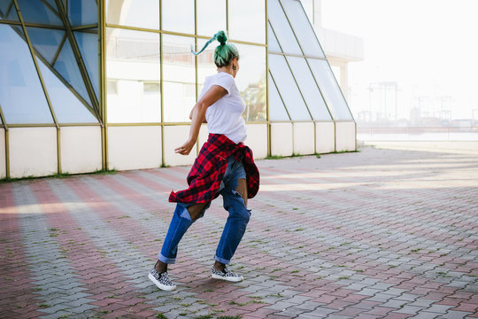 Attractive young woman in a stylish look and green hair dancing freely on urban background