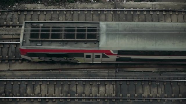 Top view on railroad tracks with double deck passenger mid distance train slowly passing by in central lane from left to right. Slow motion 60fps. Commuting concept