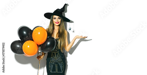 Halloween party girl. Sexy witch holding black and orange air balloons. Beautiful young woman in witches hat and costume