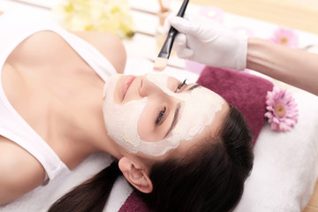 Obraz na płótnie Canvas Young girl is enjoying facial procedure at beauty salon. She is lying and getting clay mask with pleasure