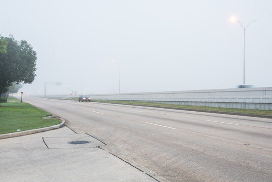Busy traffic on frontage road and freeway during foggy morning in Texas, USA. Traffic sign and car motion blurred. Driving with caution in bad weather. Hazy transportation hazard. Severe weather theme