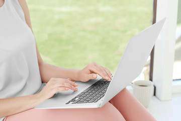 Young woman using laptop for searching information in internet on window sill