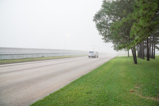 Morning foggy city frontage road, traffic sign and car motion in Humble, Texas, USA. Driving with caution in bad weather. Hazy transportation hazard. Severe weather theme concept background. Rear view