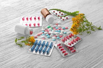 Blisters, bottles with colorful pills and herbs on wooden background