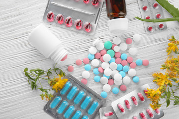 Blisters, bottles with colorful pills and herbs on wooden background