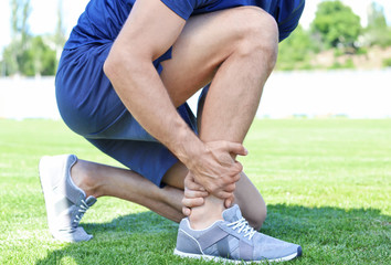 Young man suffering from pain in leg, outdoors