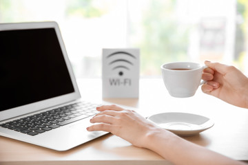 Woman holding cup of coffee while working on laptop in hotel lobby