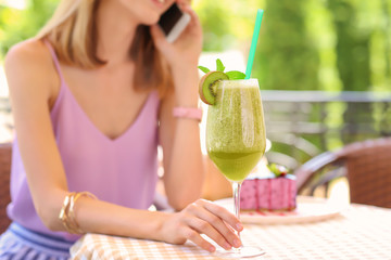 Beautiful young woman with fresh smoothie talking on mobile phone in cafe