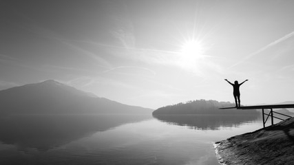 Female figure silhouette with open arms stands on the springboard for a jump into the water.  Black...