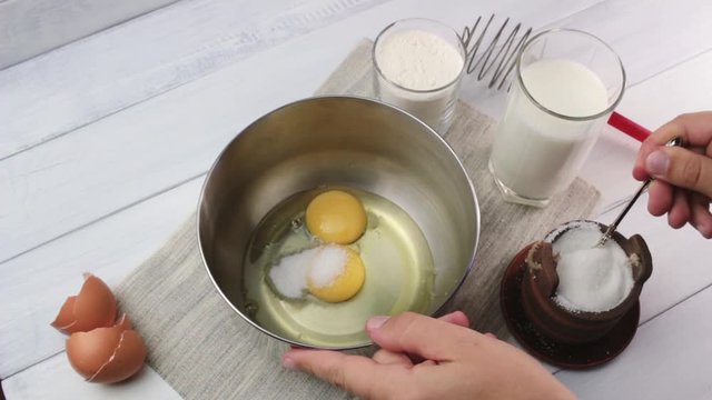 Human hand adding sugar to the broken egg in the steel bowl, making sweet batter for pancakes