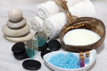 Obraz na płótnie Canvas A set for Spa procedures with coconut milk rejuvenating milk, stones and blue bath salt is located on the white marble countertop.