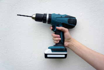 Electric screwdriver in hand, white wall background.