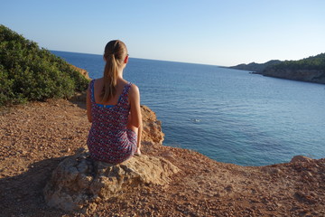 Fototapeta na wymiar Tourist blonde girl looking at the beach Sa Caleta or Bou Nou in Ibiza island, Spain. 