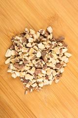 Pile of chopped roasted almond pieces on a wood background