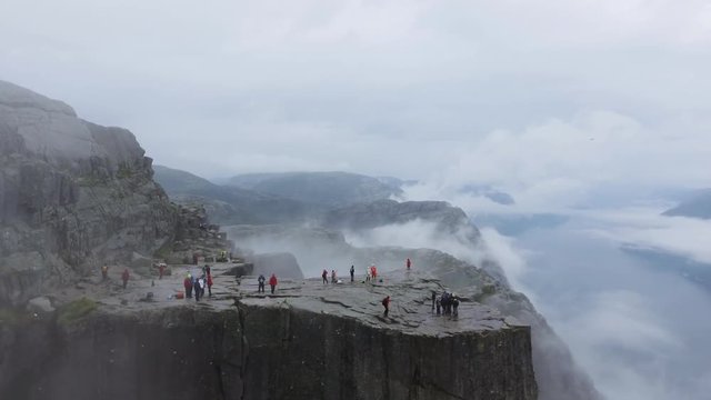 Aerial shot magnificent landmark in Norway, Europe. Tourists walk on large rock. Preikestolen Landscape, Prekestolen, Preacher's Pulpit or Pulpit Rock. Amazing scenery, mountains, steep cliffs in fog