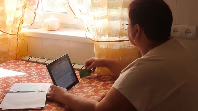 Portrait of older woman with credit card and touch screen tablet. People, technology and shopping online concept - happy woman sitting a with tablet pc computer and bank card at home.