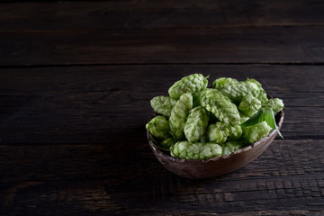 cones of hops in a wooden bowl on a wooden background