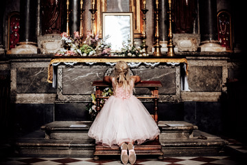 a LIttle blonde girl in a pink dress praying near the altar in the temple. View from behind.the...