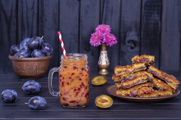 Homemade plum pie in plate, plum smoothies and raw plums on black wooden background